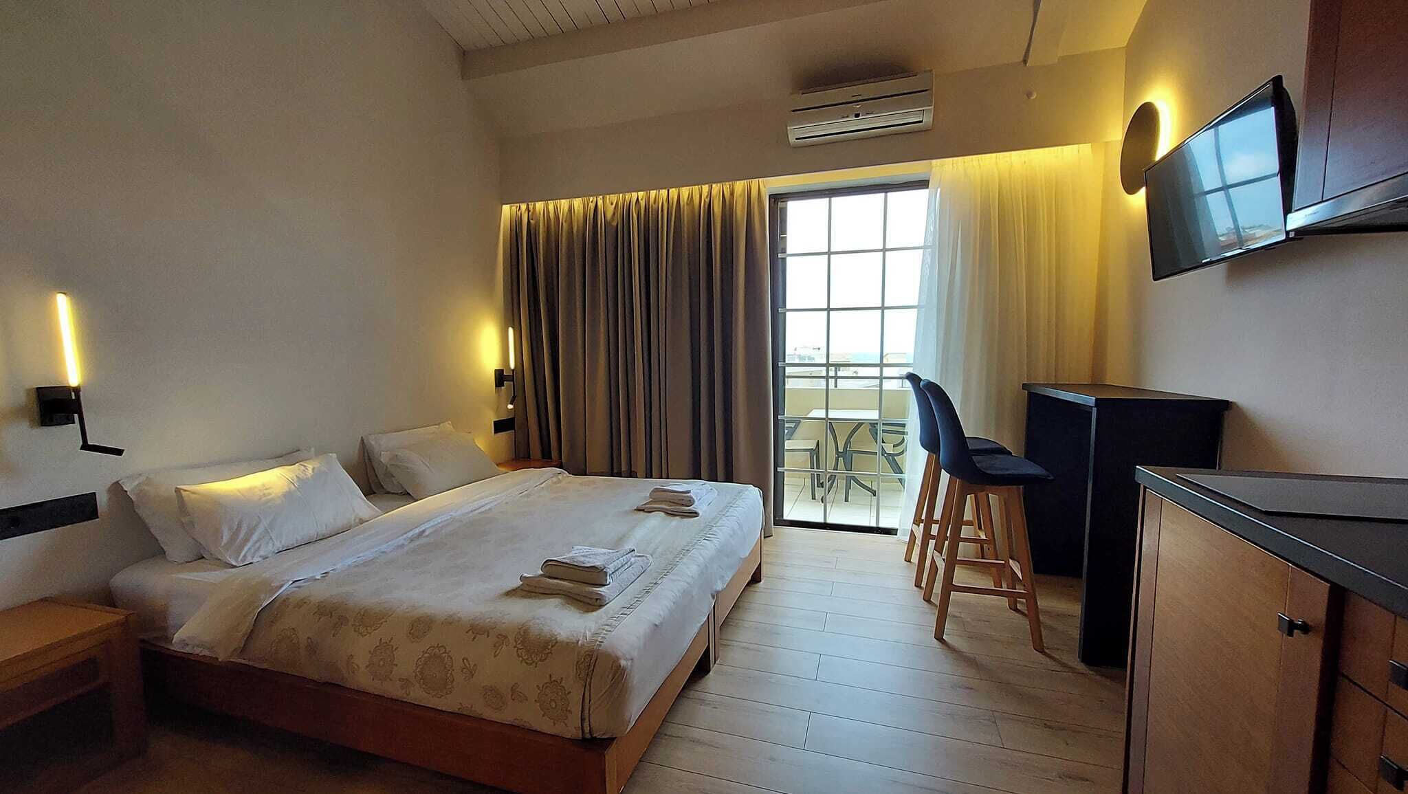 Une chambre d’hôtel comprenant un lit, un bureau, une chaise, une télévision et un balcon avec une table et des chaises.