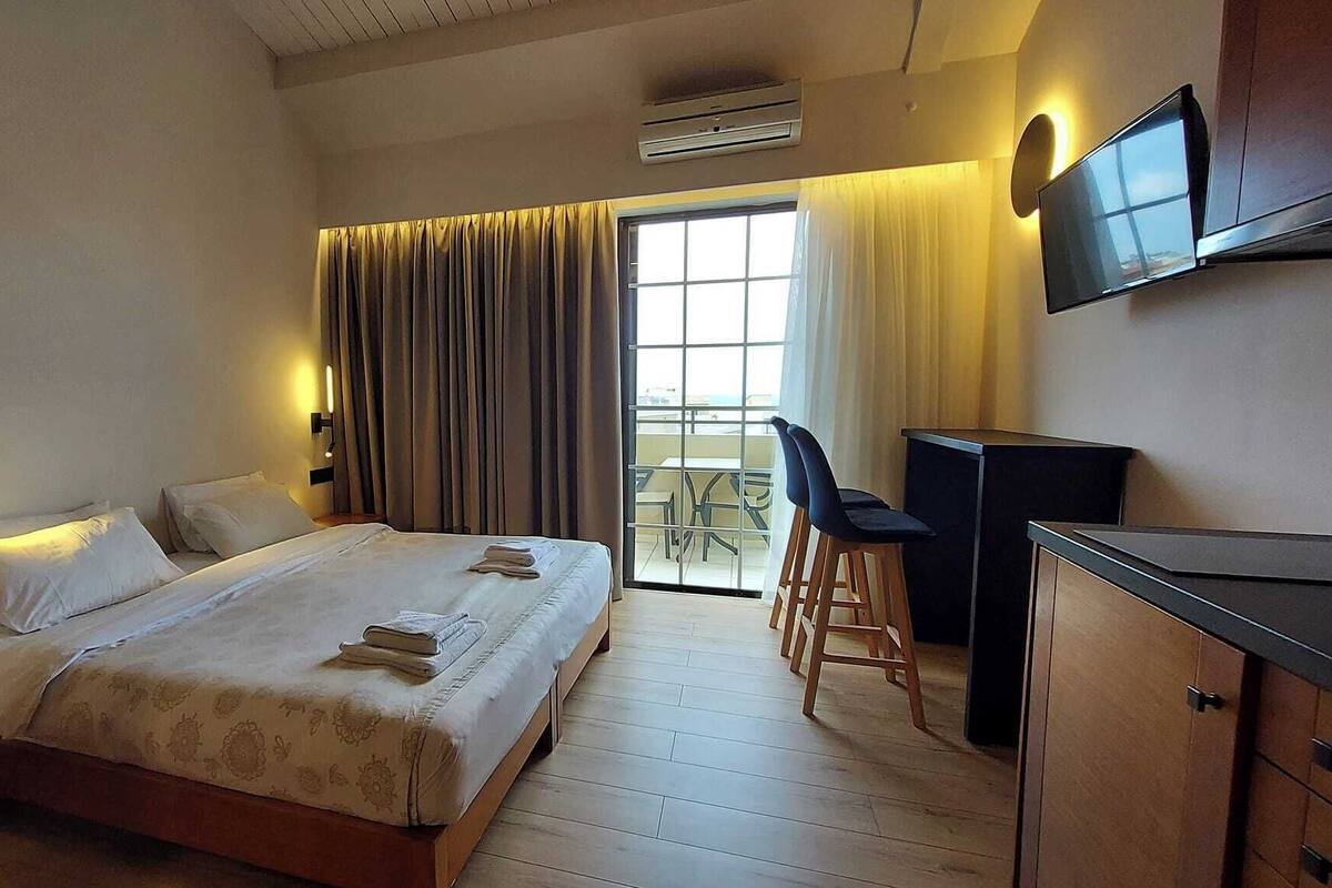 Une chambre d’hôtel comprenant un lit, un bureau, une chaise, une télévision et un balcon avec une table et des chaises.