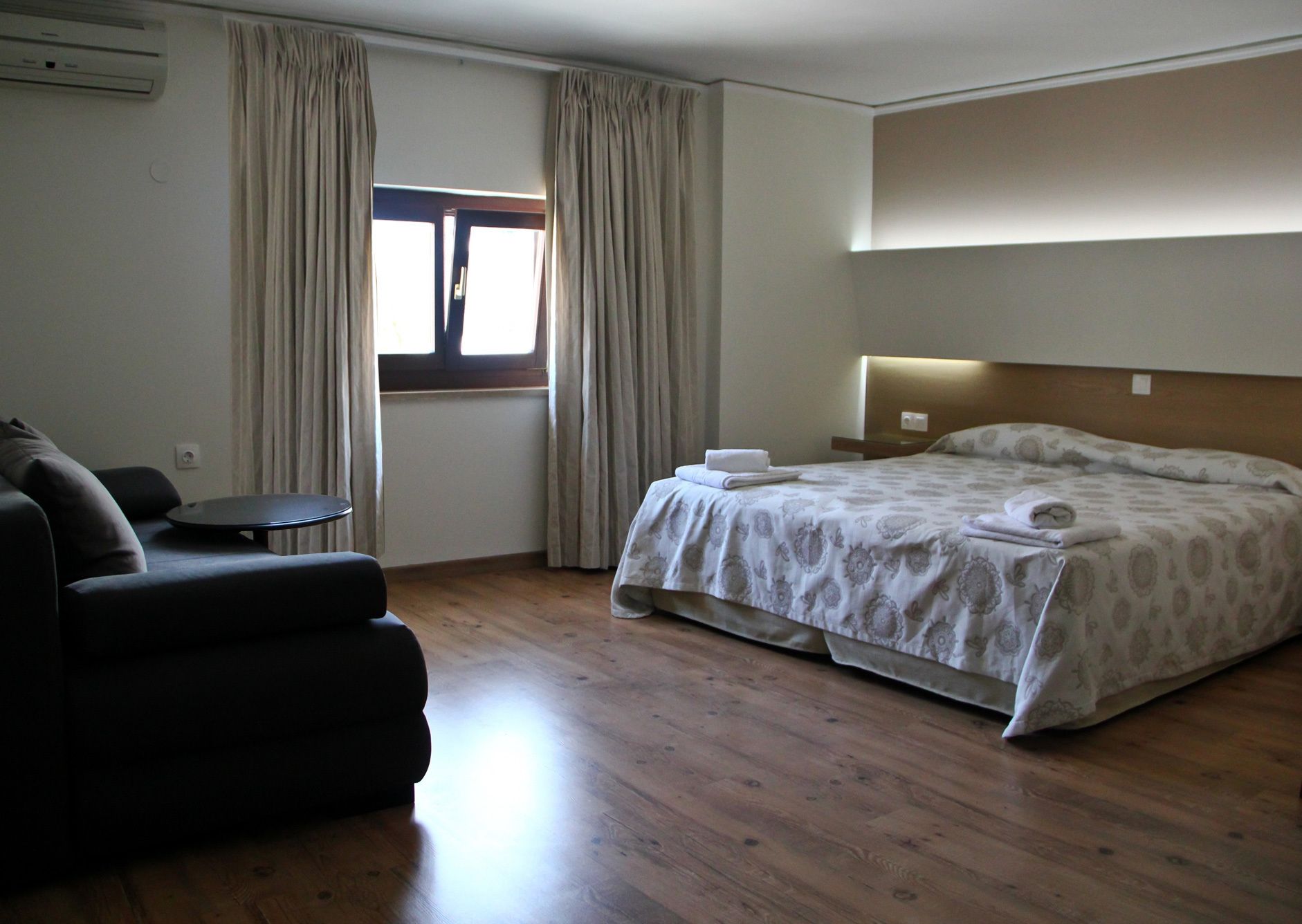 A hotel room with a bed, a sofa, a small table, and a window with curtains.