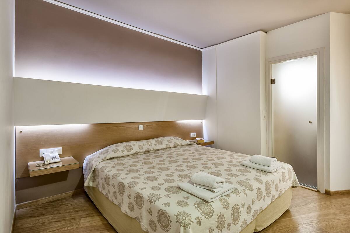 A neatly made bed with a patterned bedspread and two towels, a bedside table with a phone, and a nightstand with a lamp.