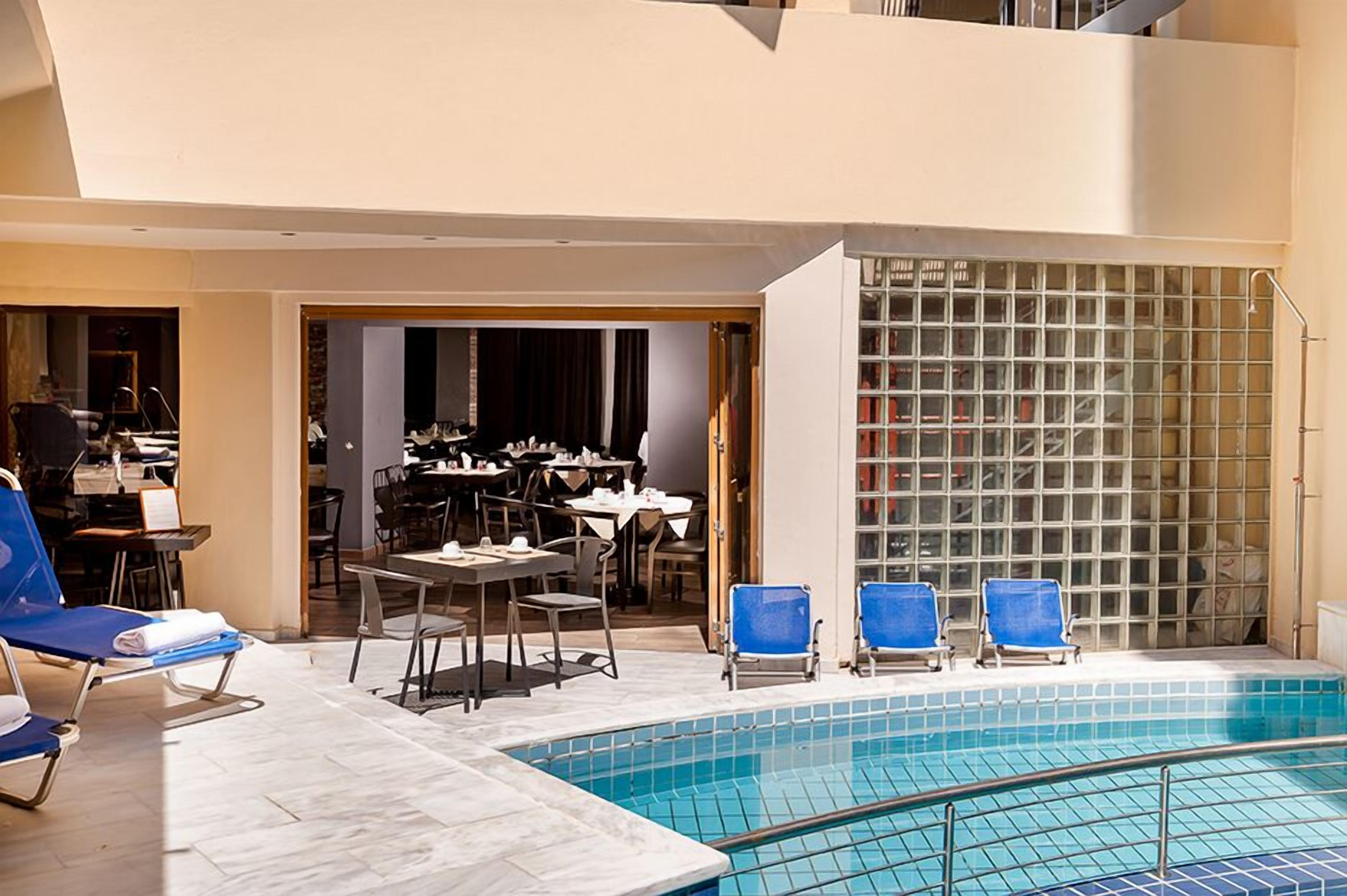 Une piscine intérieure avec des chaises longues bleues, un espace repas avec des tables et des chaises, et une cloison vitrée.