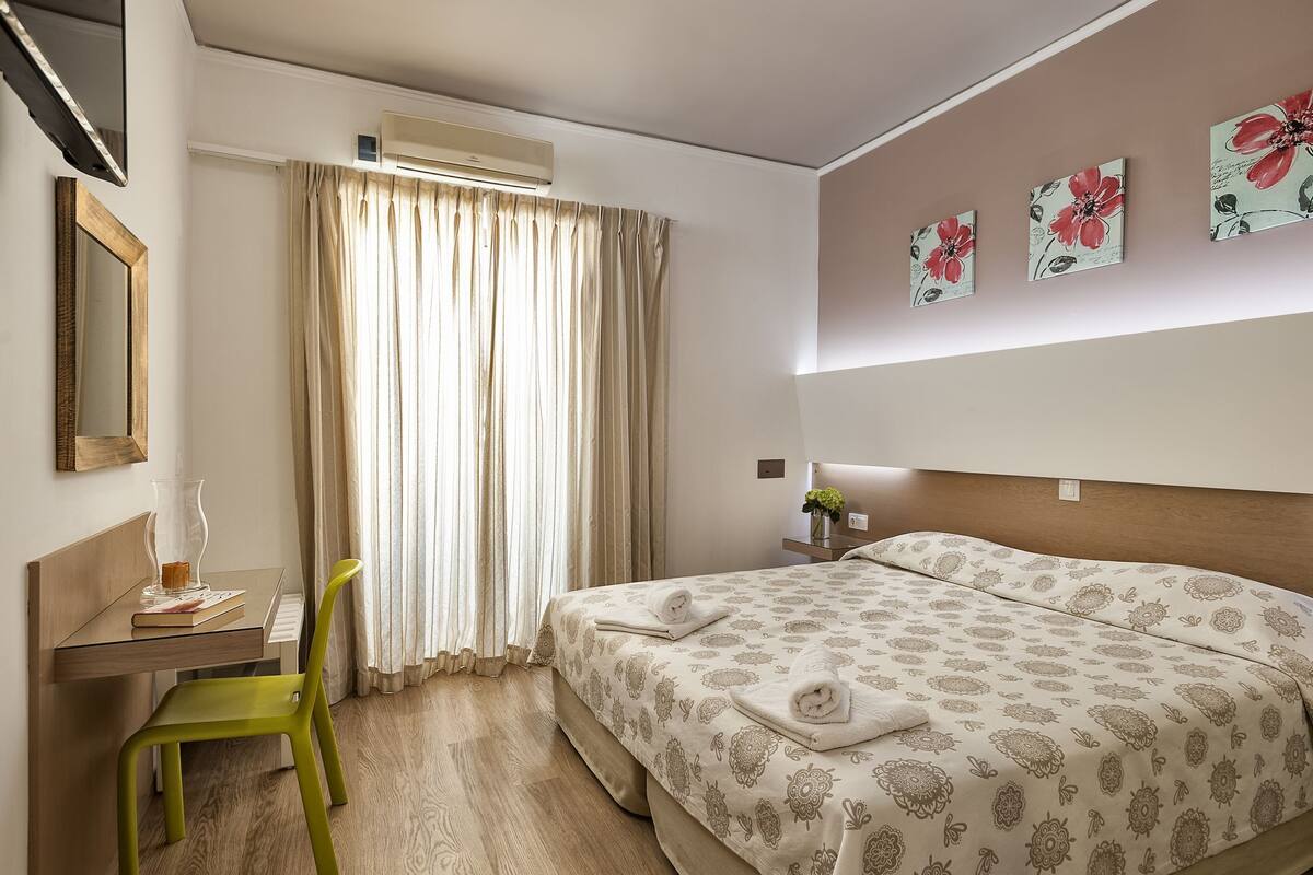 Une chambre d’hôtel comprenant un lit, un bureau avec une chaise, une fenêtre avec des rideaux et des œuvres d’art murales.