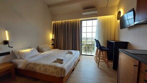 Habitación de hotel con cama, escritorio, silla, televisor y balcón con mesa y sillas.