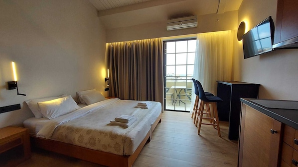 Habitación de hotel con cama, escritorio, silla, televisor y balcón con mesa y sillas.