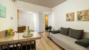 A modern living room with a sofa, a dining table with chairs, and a kitchen area in the background.