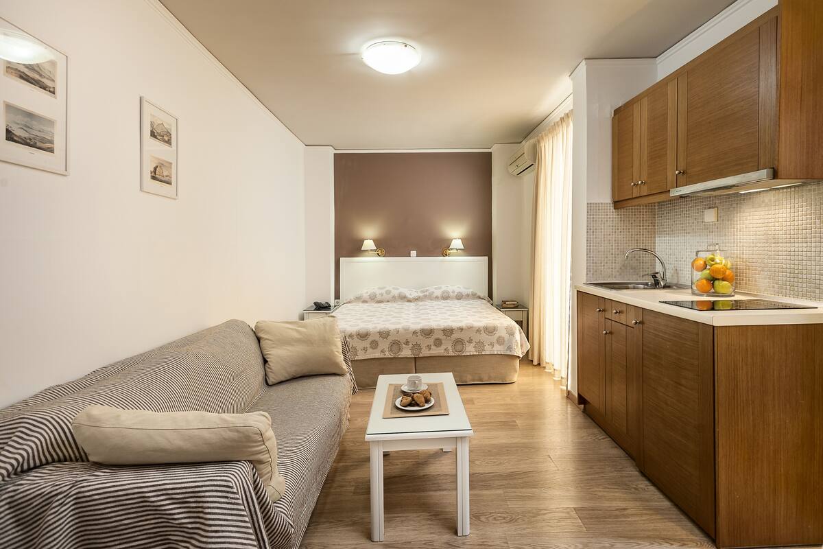A compact room with a bed, a sofa, a small table, and a kitchenette.