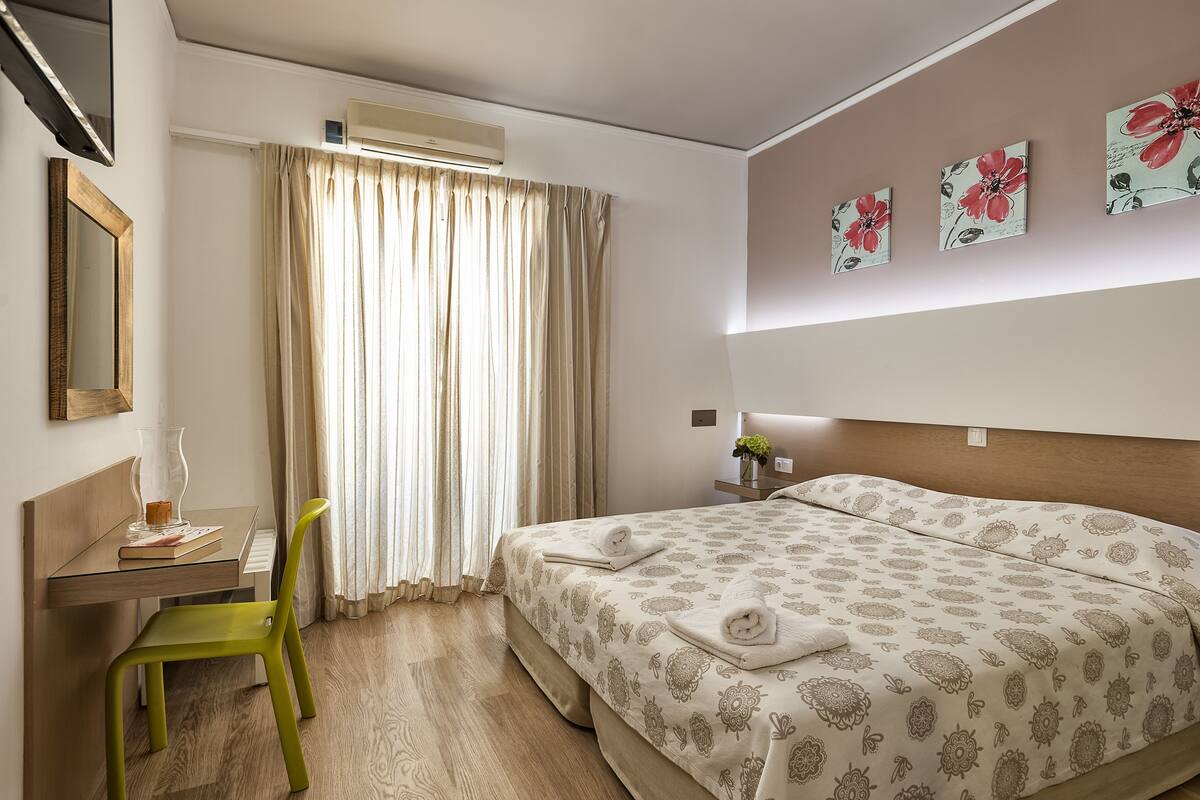 A hotel room with a bed, a desk, a chair, and a window with curtains.