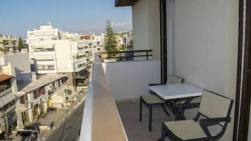 A balcony with a table and chairs, overlooking a street with buildings and a clear sky.