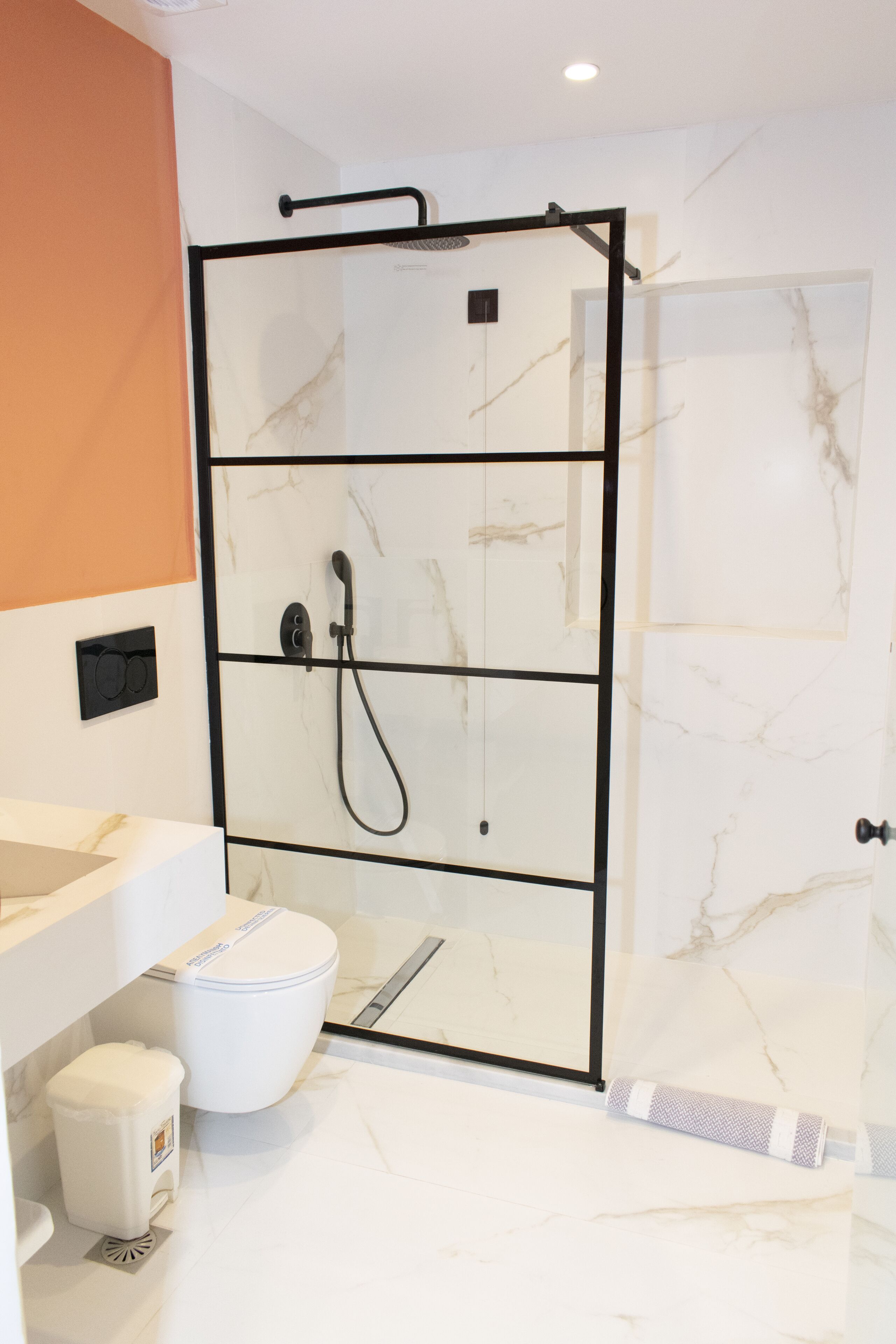 A modern bathroom with a glass-enclosed shower, a white toilet, and a sink with a marble countertop.