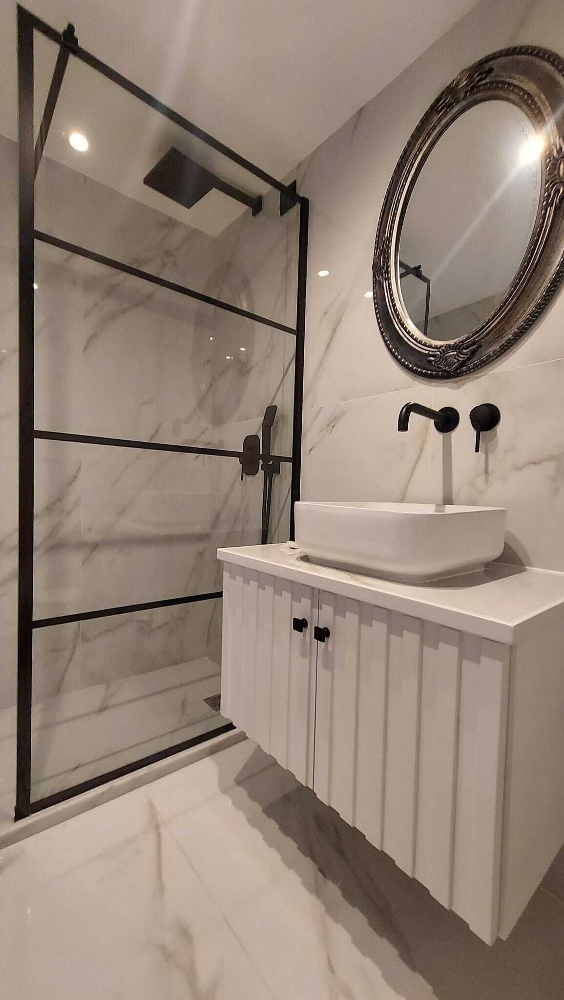 Un bagno moderno con cabina doccia in vetro, lavabo in marmo bianco e uno specchio grande.