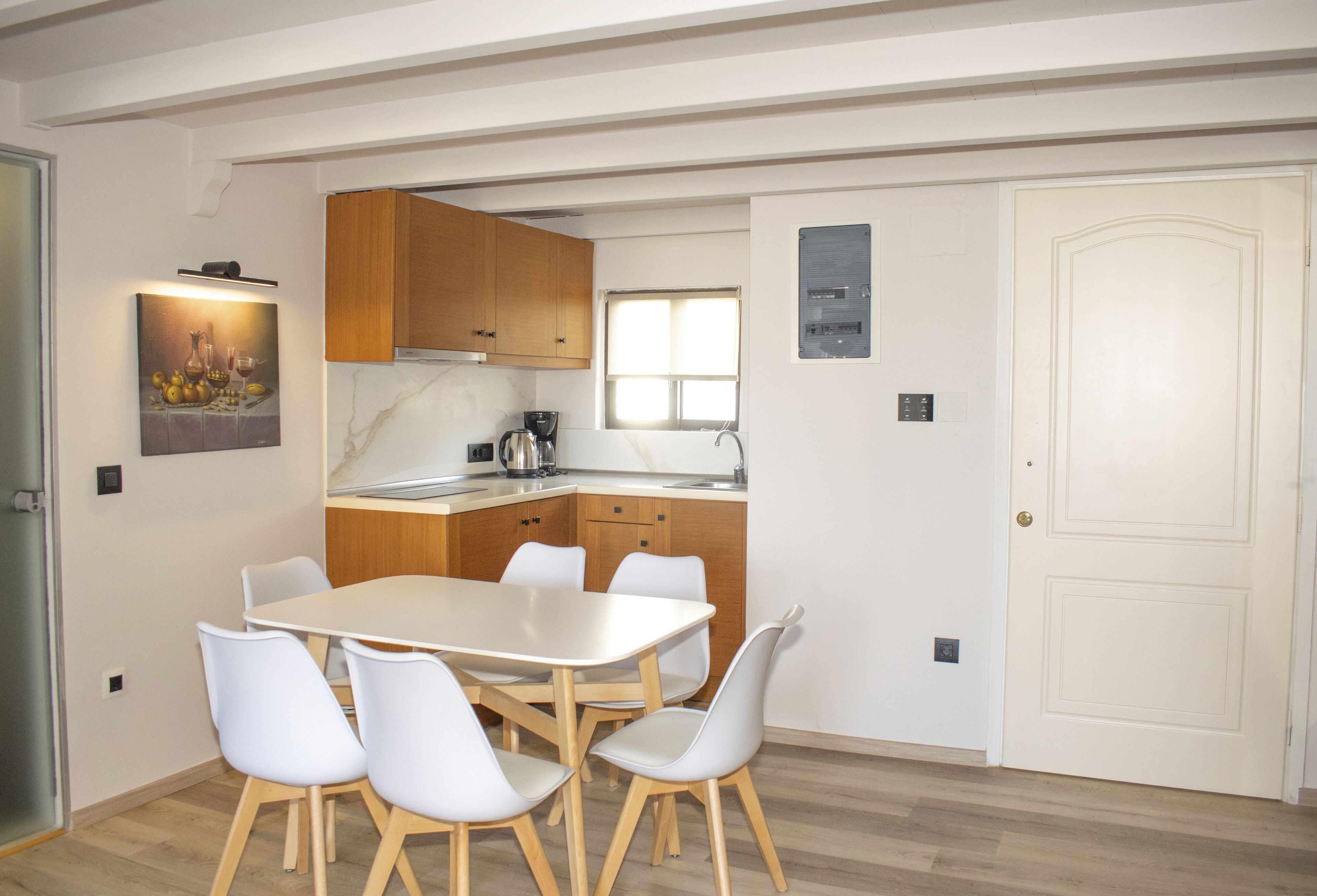 Une cuisine moderne avec des meubles en bois, un plan de travail blanc et un coin repas comprenant une table et des chaises blanches.