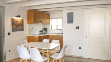 Une cuisine moderne avec des meubles en bois, un plan de travail blanc et un coin repas comprenant une table et des chaises blanches.