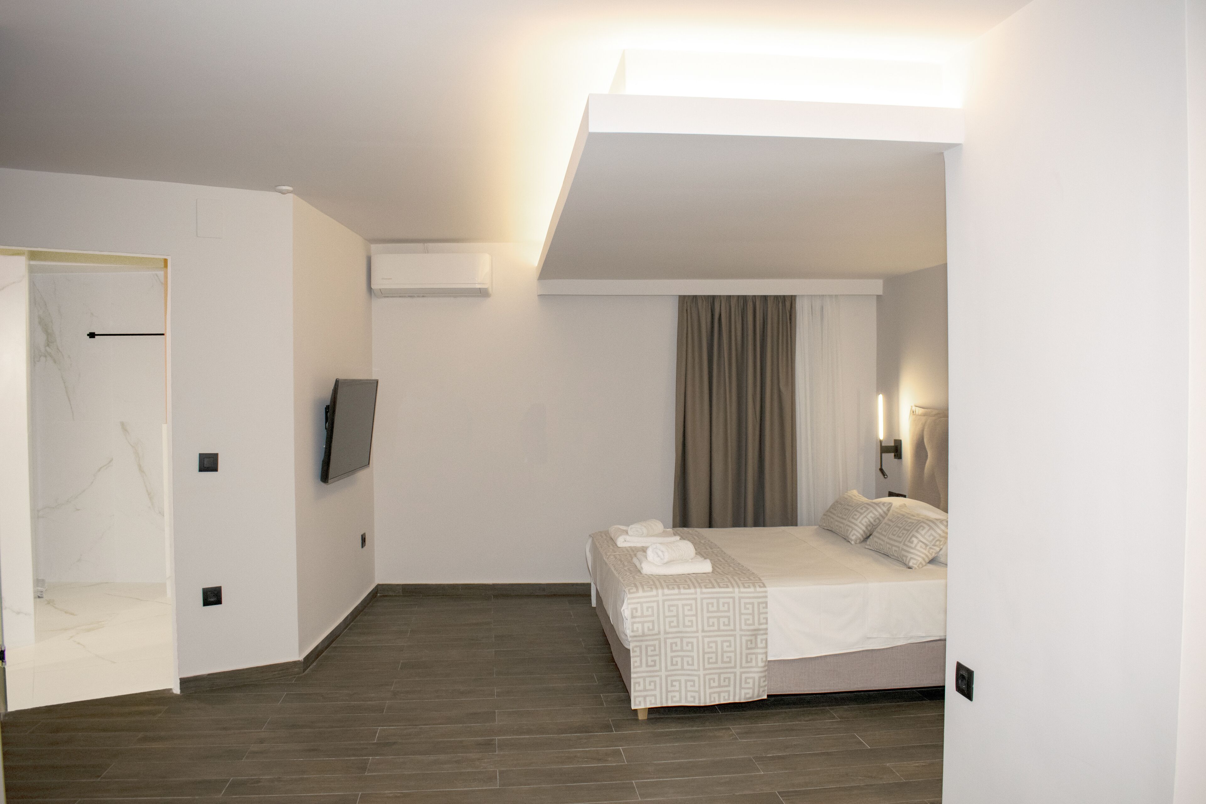 Una habitación de hotel moderna con una cama, un televisor de pantalla plana, una ventana con cortinas y suelo de madera.