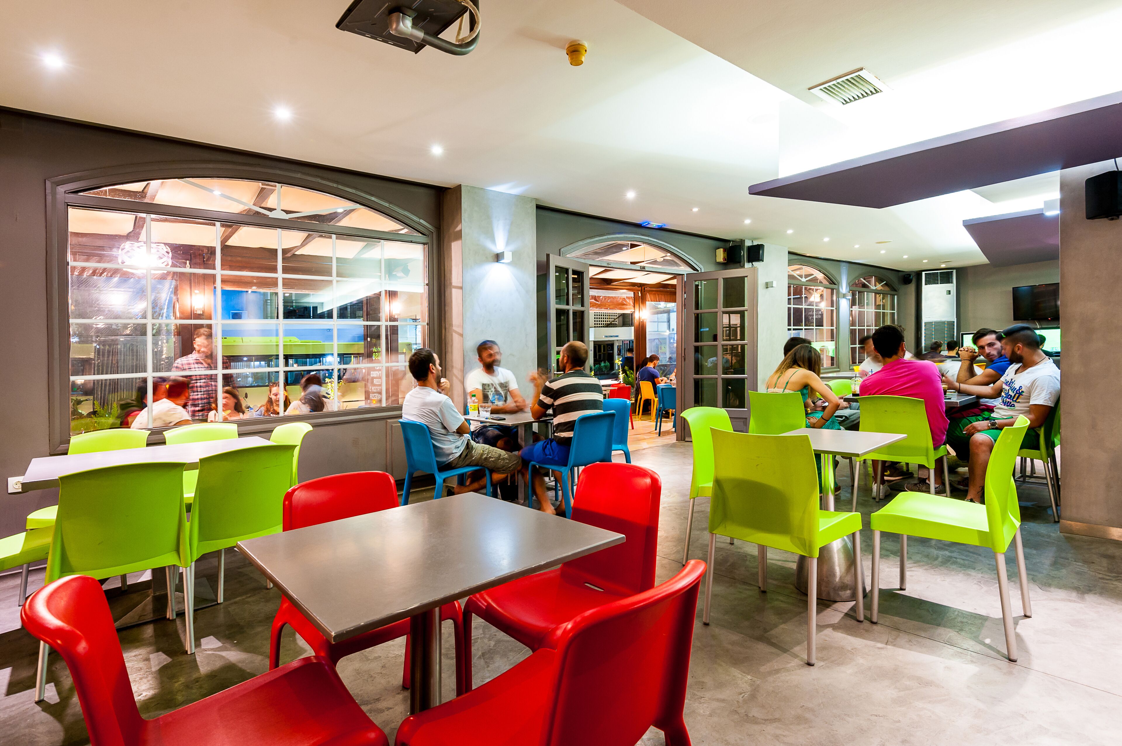 A modern dining area with green and red chairs, tables, and a large window providing a view of the outside.