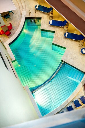 A swimming pool with blue lounge chairs and red chairs around it. - Elina Hotel Apartments (Rethymno)