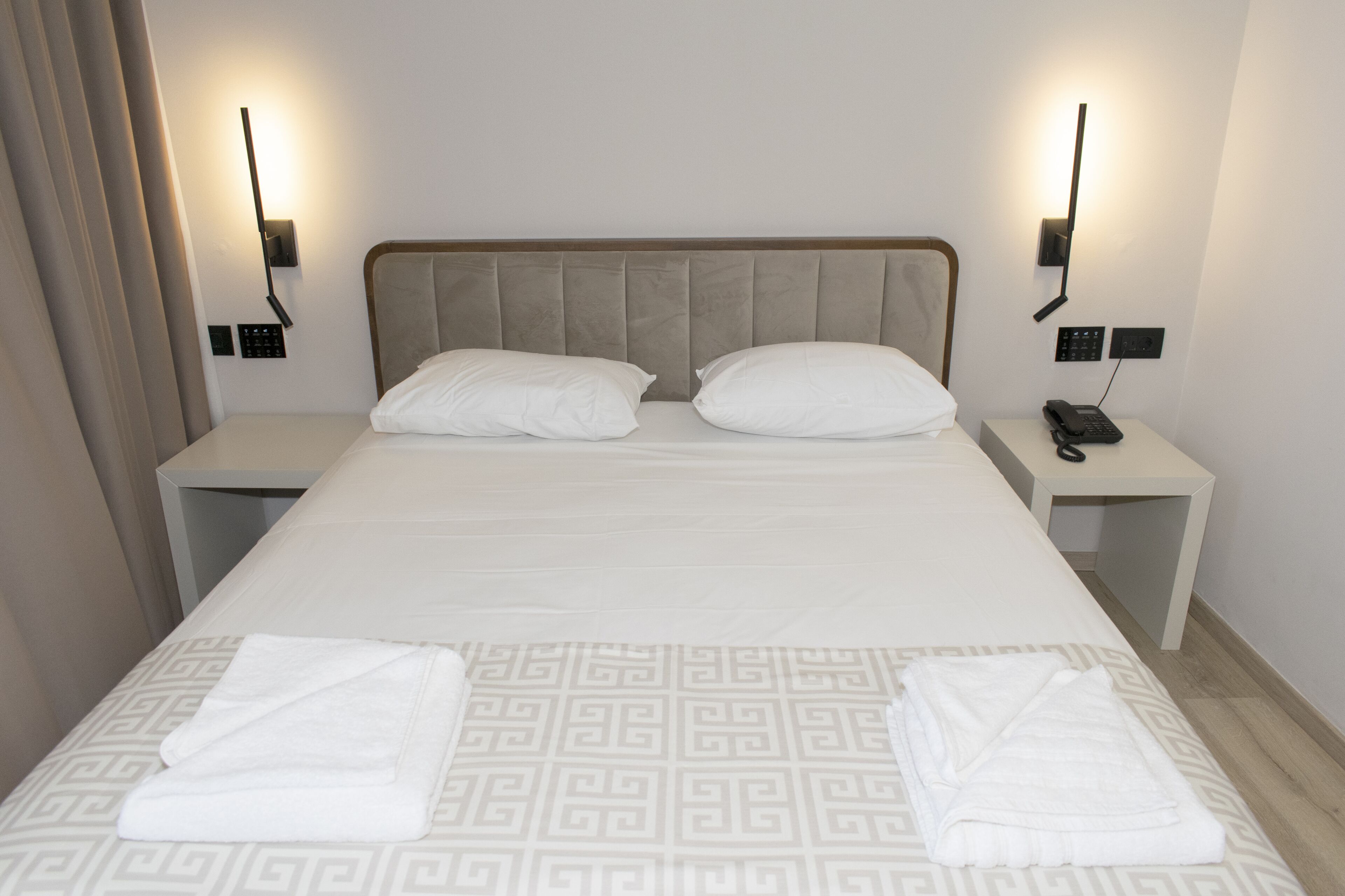 A hotel room with a large bed, two bedside tables, a telephone, and a wall-mounted light fixture.