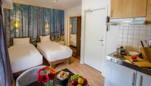 Habitació d'hotel amb dos llits, una cuineta i zona de dinar amb fruita i pastissos.