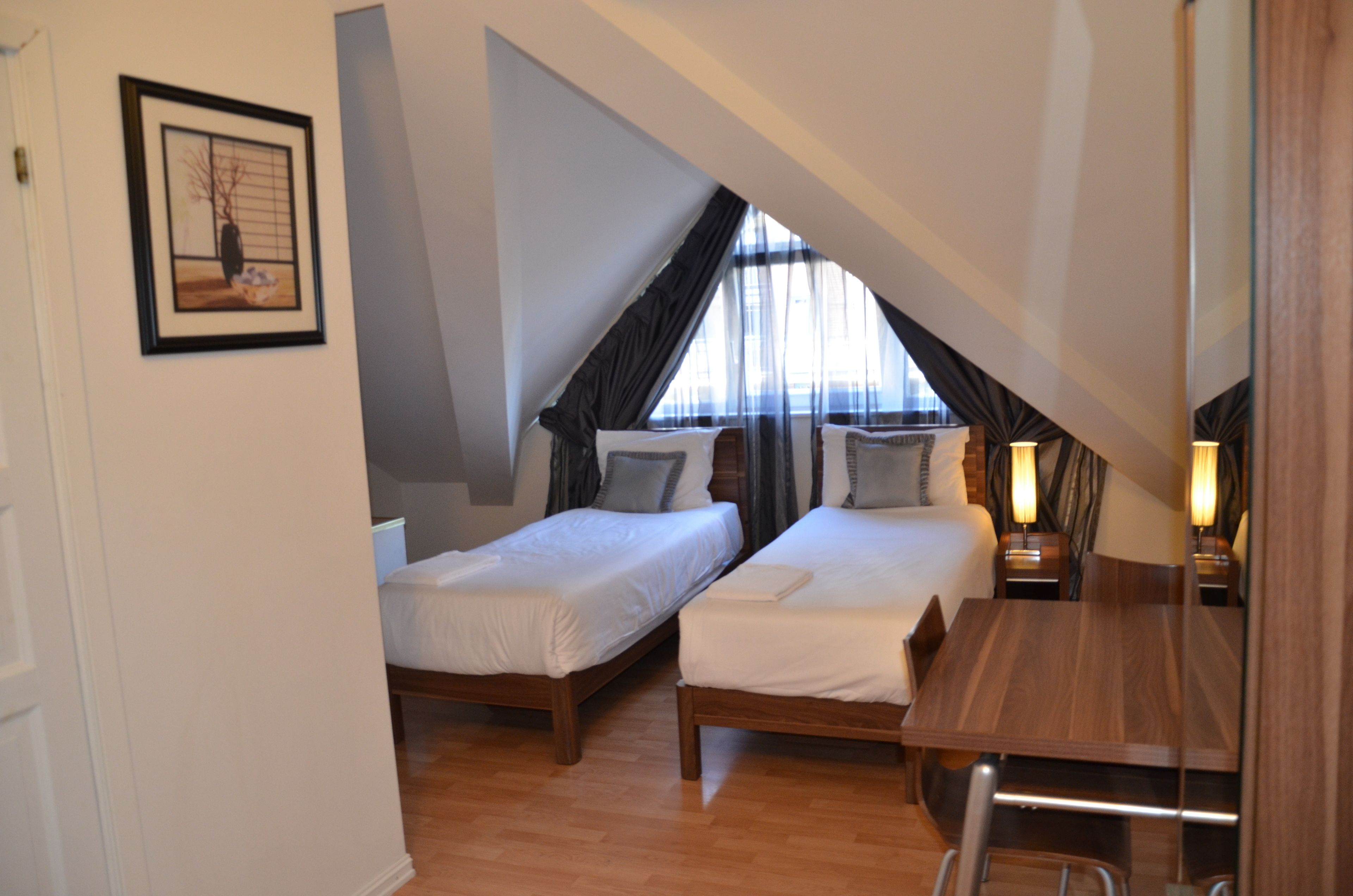 A bedroom with two single beds, a wooden table, and a window with sheer curtains.