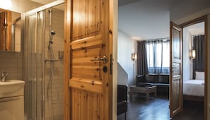 Habitació d'hotel amb una porta de fusta, un bany amb plat de banyera de vidre, un llit, un sofà i una taula petita.