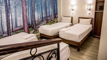 A hotel room with two beds, a large forest mural on the wall, and a wooden floor.