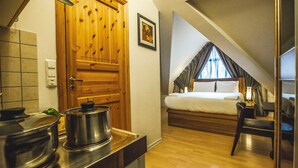 Un dormitorio pequeño con puerta de madera, cama con ropa blanca, mesita de noche y ventana con cortinas.