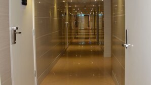 Un pasillo con piso reflectante, puertas de vidrio y una señal de salida verde.