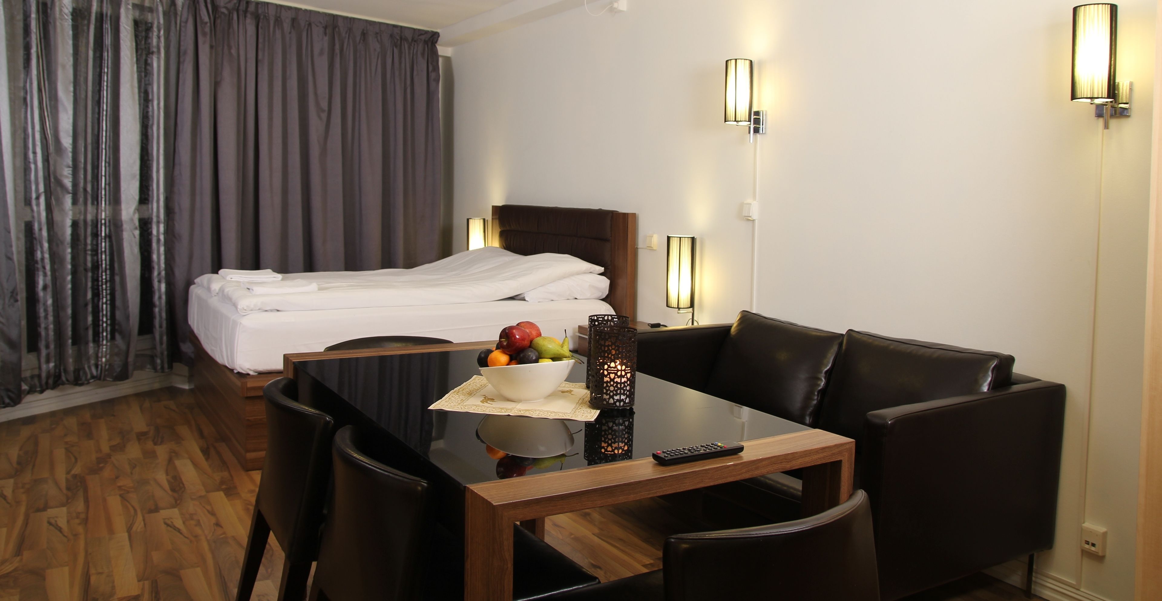 Ein Hotelzimmer mit einem Bett, einem Esstisch mit Stühlen, einer Obstschale und einer Fernbedienung.