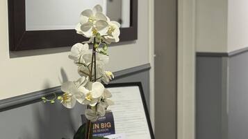Una recepción con un cartel enmarcado, una orquídea en maceta y un espejo en la pared.