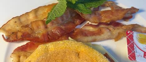 A breakfast plate with bacon, eggs, and toast, accompanied by a glass of juice and a bowl of fruit.