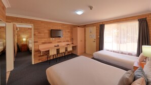 Una habitación de hotel con cama, escritorio con sillas, televisor y ventana con cortinas.