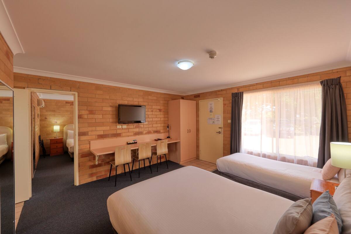 A hotel room with a bed, a desk with chairs, a television, and a window with curtains.