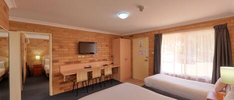 A hotel room with a bed, a desk with chairs, a television, and a window with curtains.