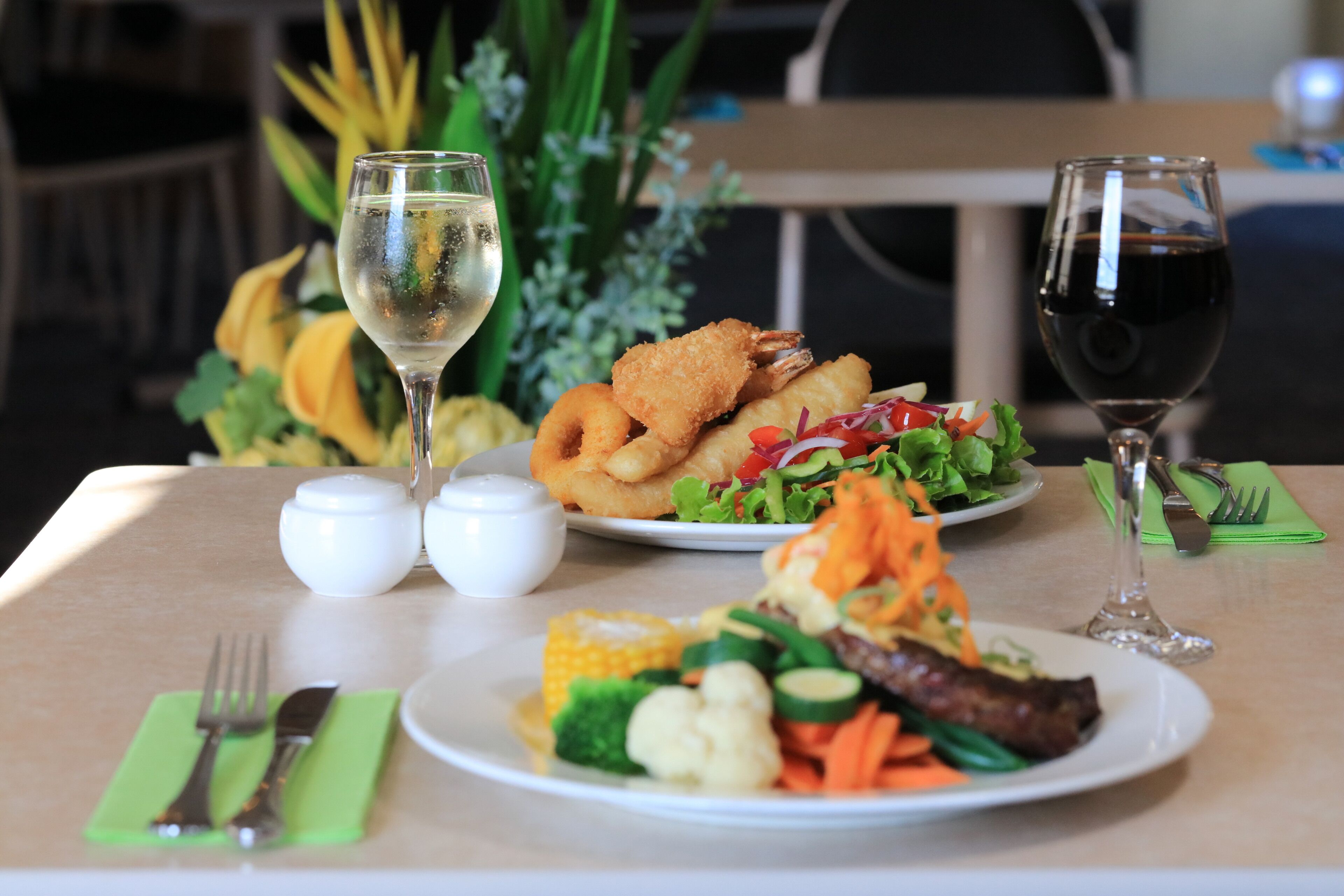 Una mesa servida con platos de comida, dos copas de vino y un mantel individual verde.