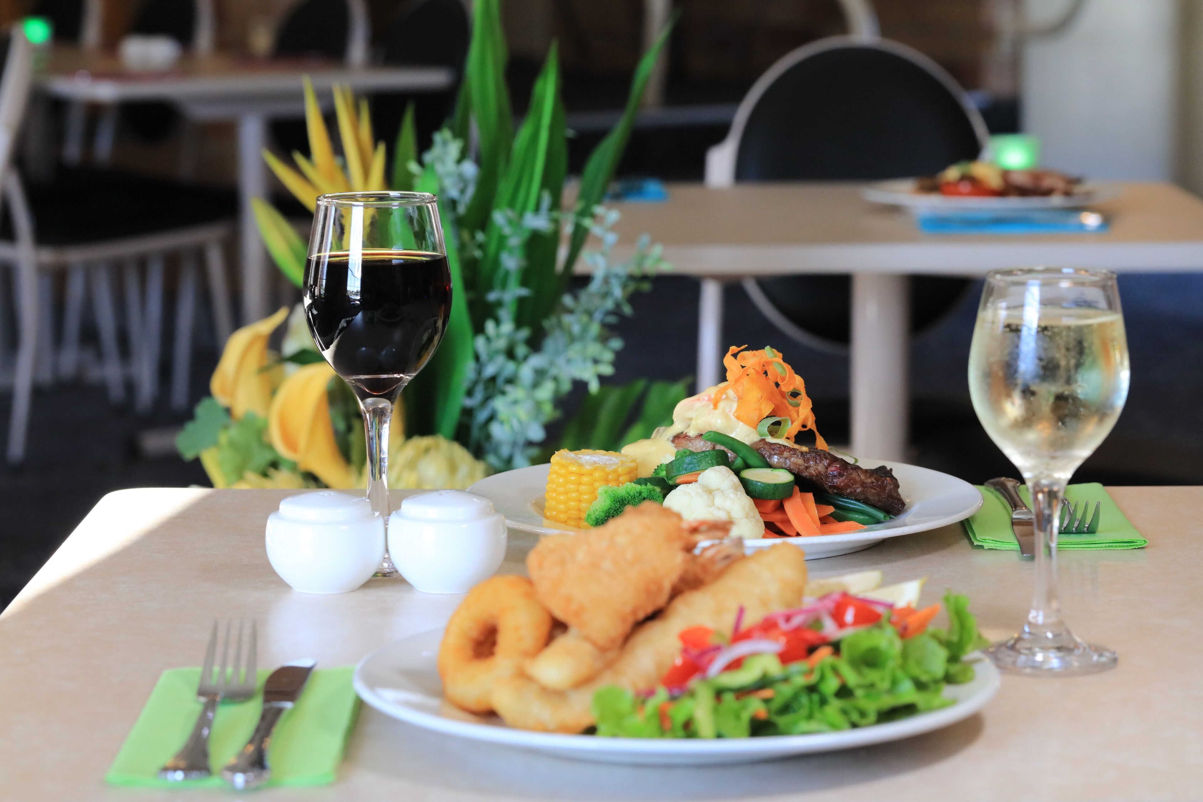 Une table à manger avec des assiettes remplies de nourriture, deux verres de vin et une serviette verte.