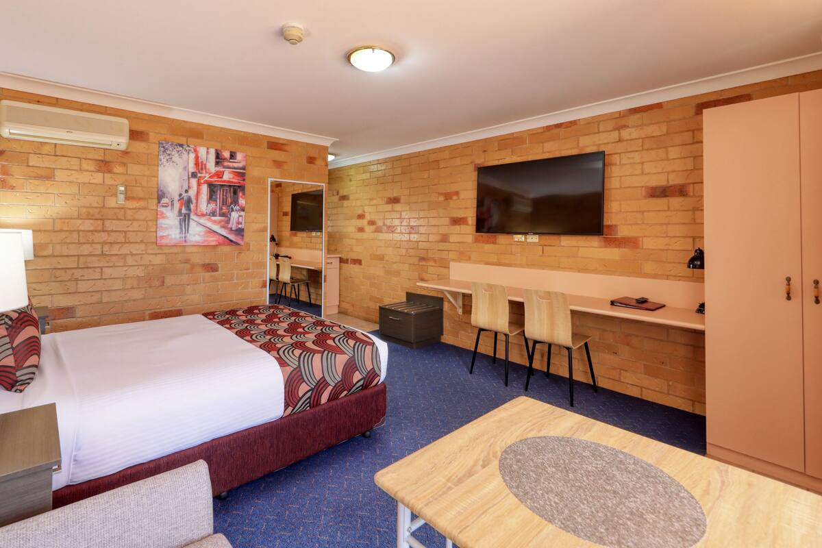 A hotel room with a bed, desk, chairs, a TV, and a wardrobe.