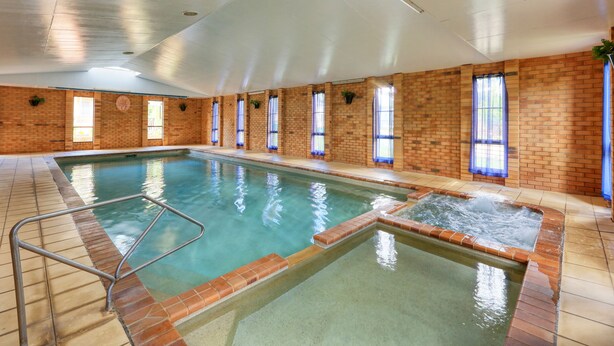 Una piscina interior con suelo de baldosas, un jacuzzi y paredes de ladrillo con ventanas.