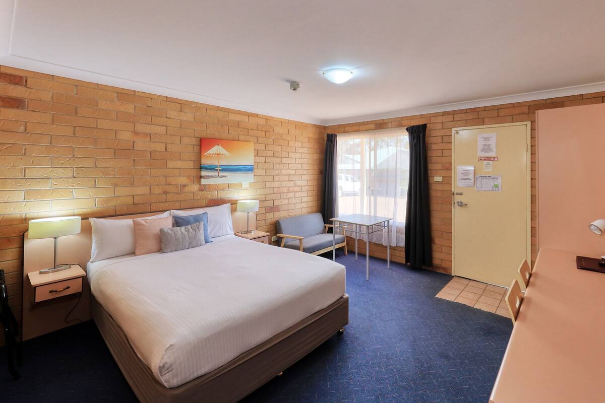 A hotel room with a large bed, a desk with a lamp, a chair, a small table, and a TV.