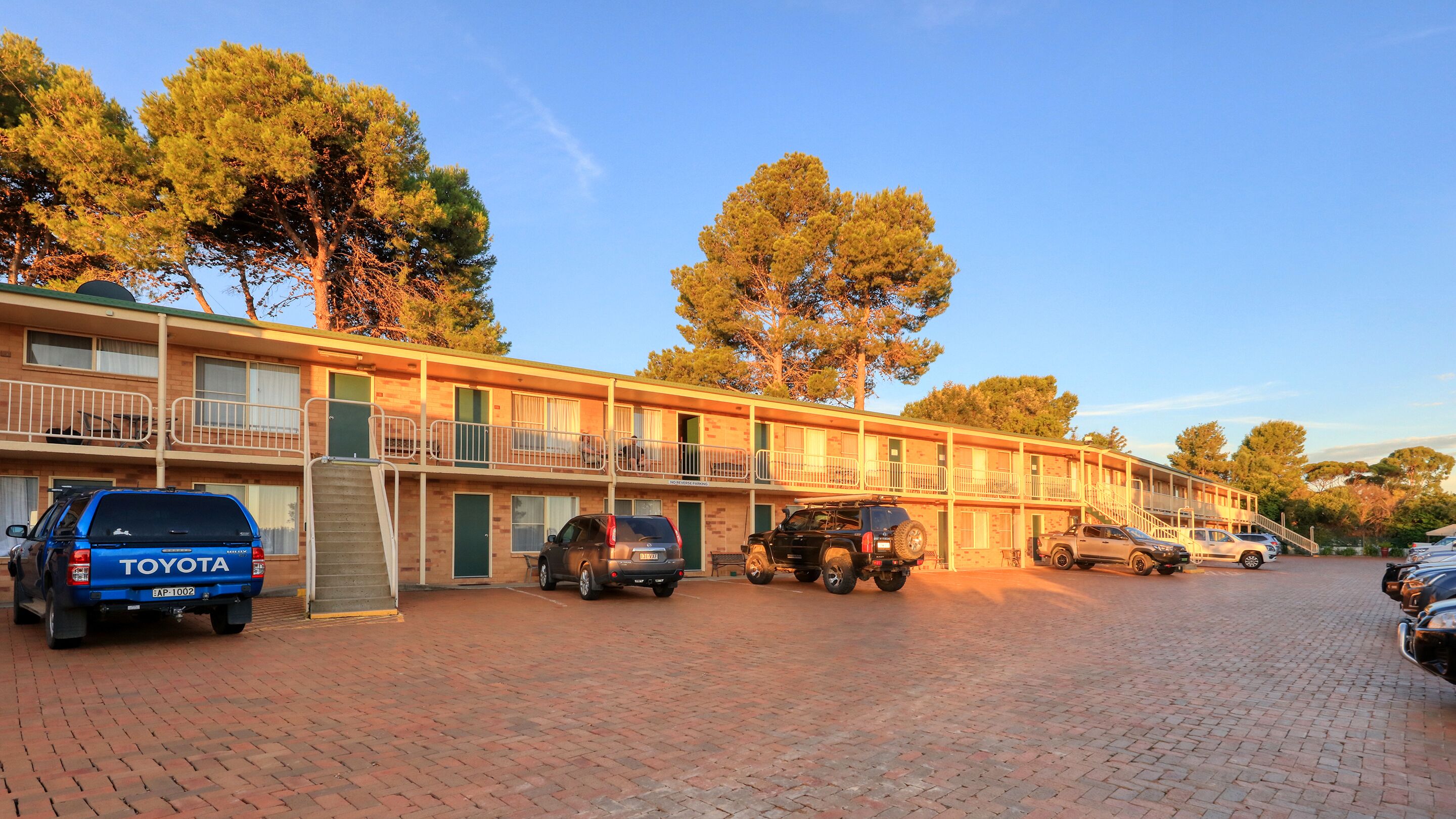 A motel with multiple floors, outdoor parking, and a brick-paved driveway.
