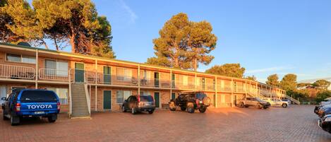A motel with multiple floors, outdoor parking, and a brick-paved driveway.