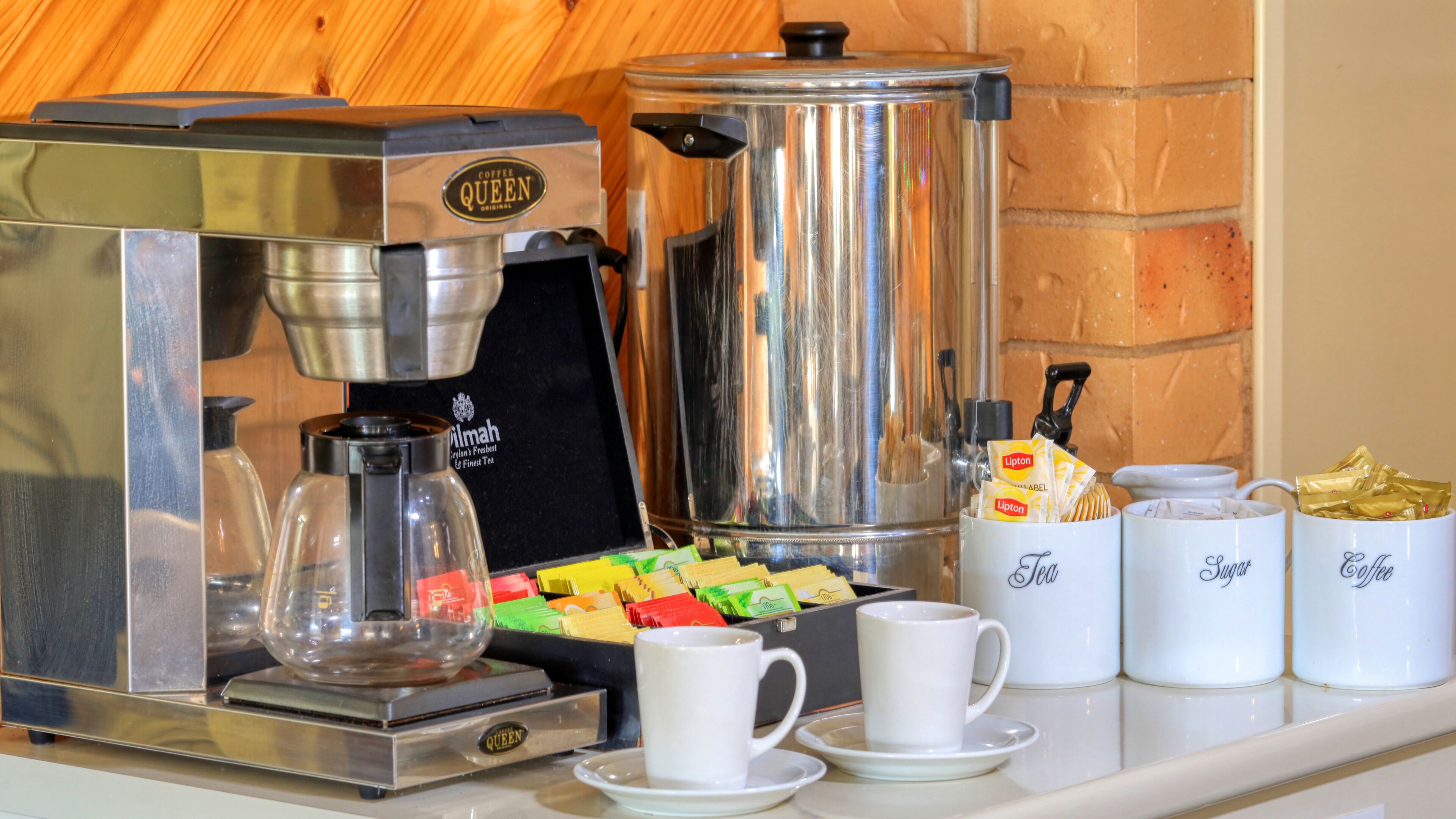 A coffee station with a coffee maker, a tea dispenser, and containers of Lipton tea and sugar.