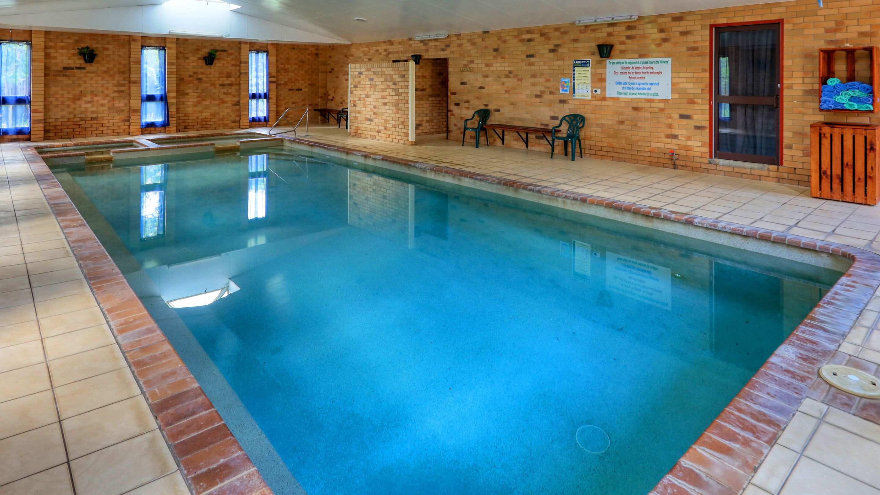 An indoor swimming pool with tiled walls and a bench near the pool.