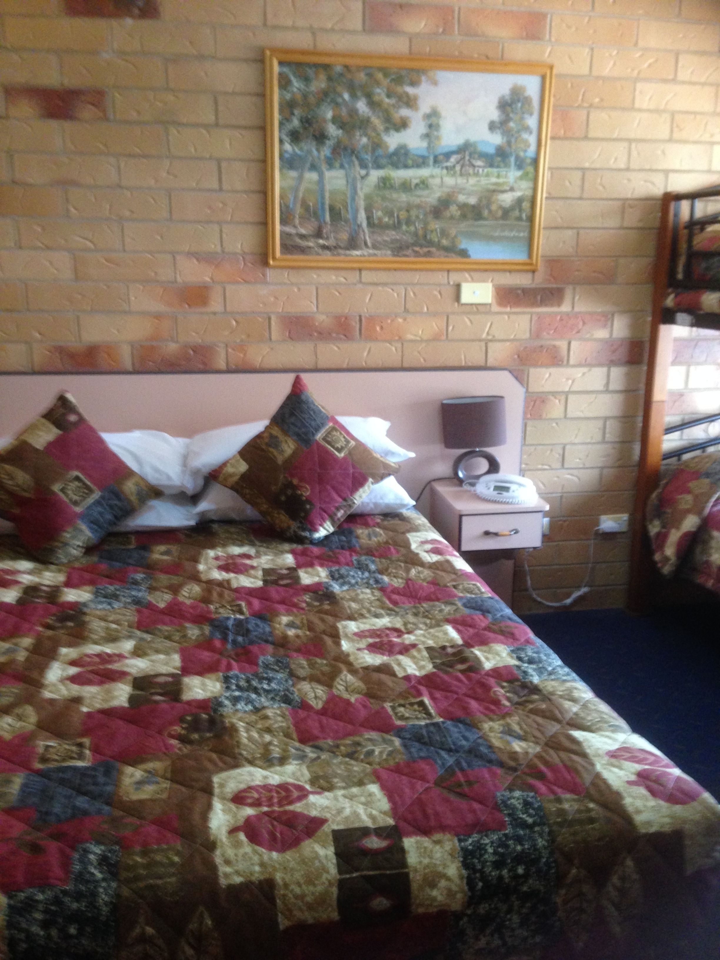 Ein Bett mit Tagesdecke, ein Nachttisch mit Telefon und ein Gemälde an der Wand.