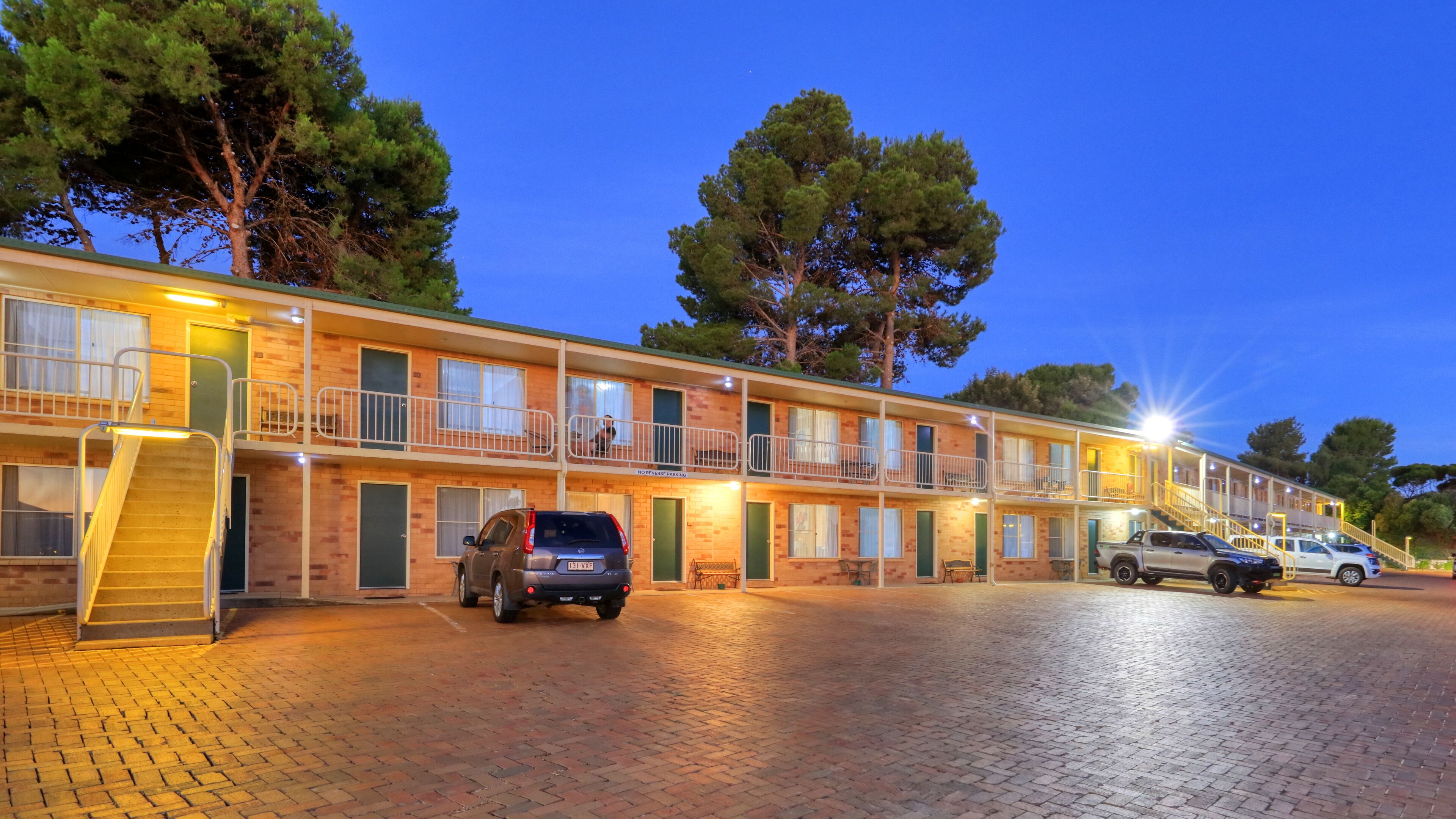 A motel with a brick facade, multiple balconies, and a paved driveway.