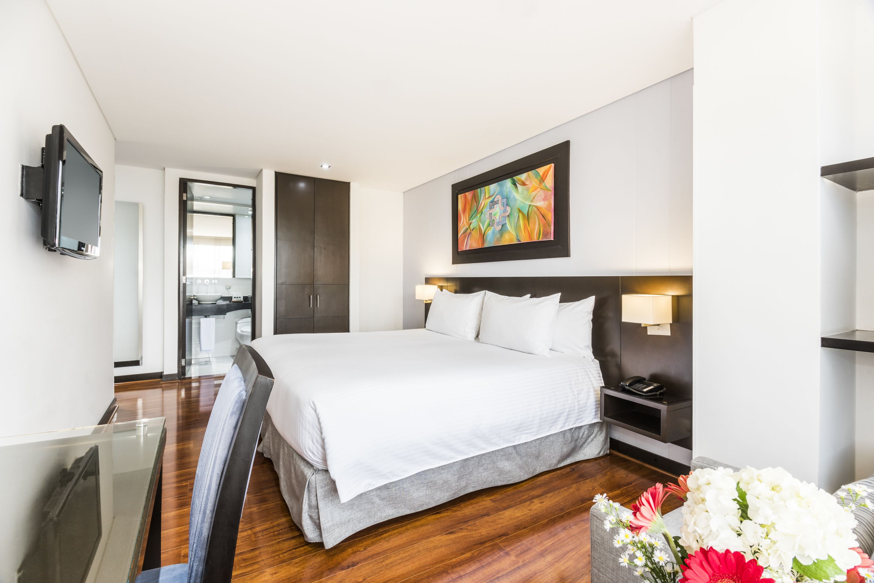 Una habitación de hotel moderna con una cama grande, mesita de noche, televisor y un cuadro en la pared.