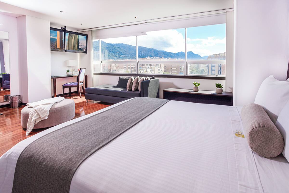 A modern hotel room with a large bed, a desk, and a view of mountains.