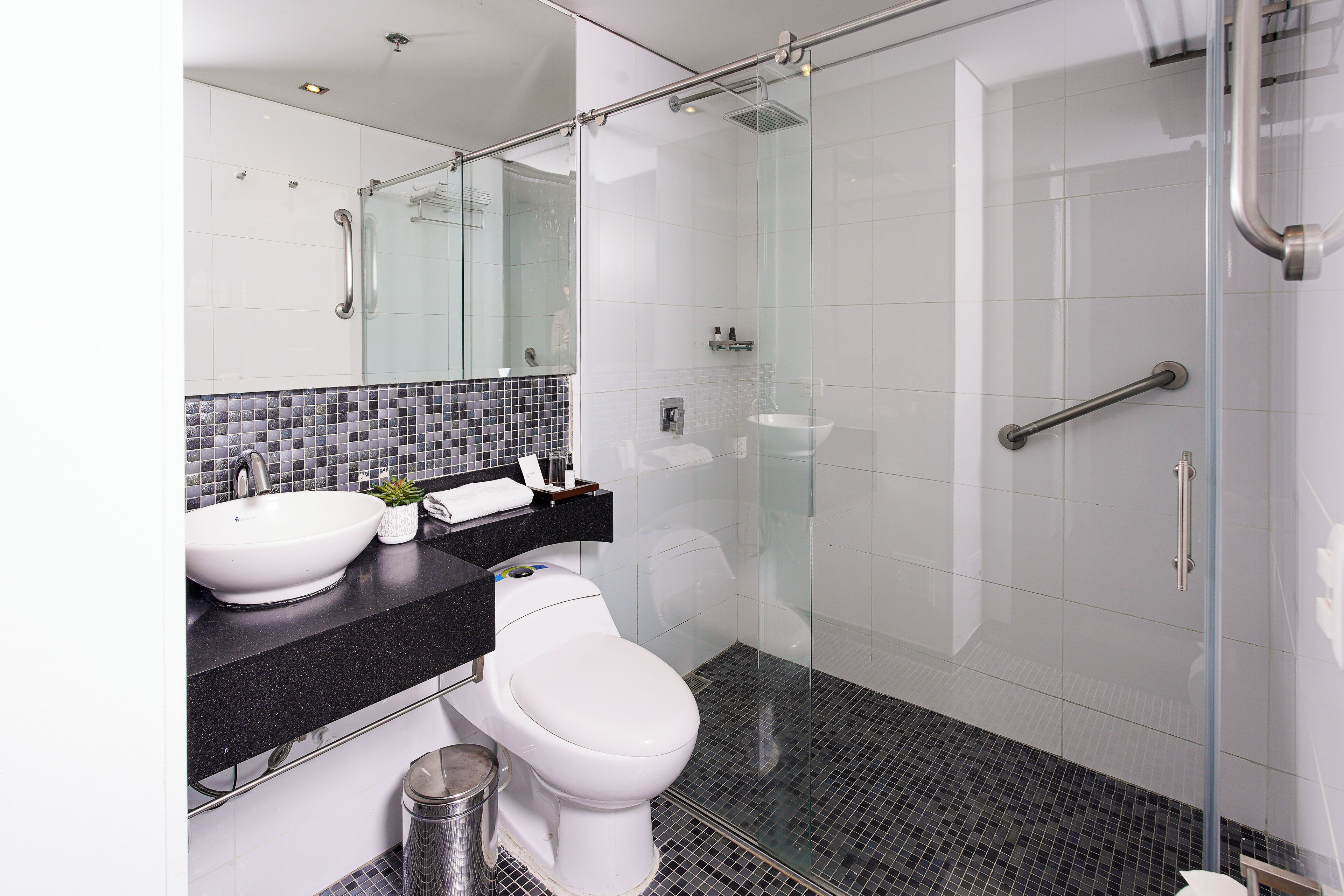 A modern bathroom with a glass-enclosed shower, a white toilet, and a black countertop with a sink and mirror.