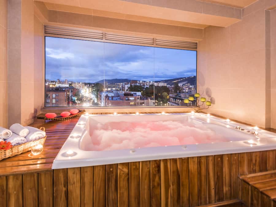 Spa-huone, jossa on suuri ikkuna, poreallas, pyyhkeet ja koristeellinen lamppu.