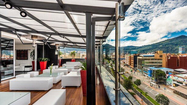 A modern lounge area with white sofas and glass tables, large windows offering a city view. - One Sixteen Hotel (Bogotá)