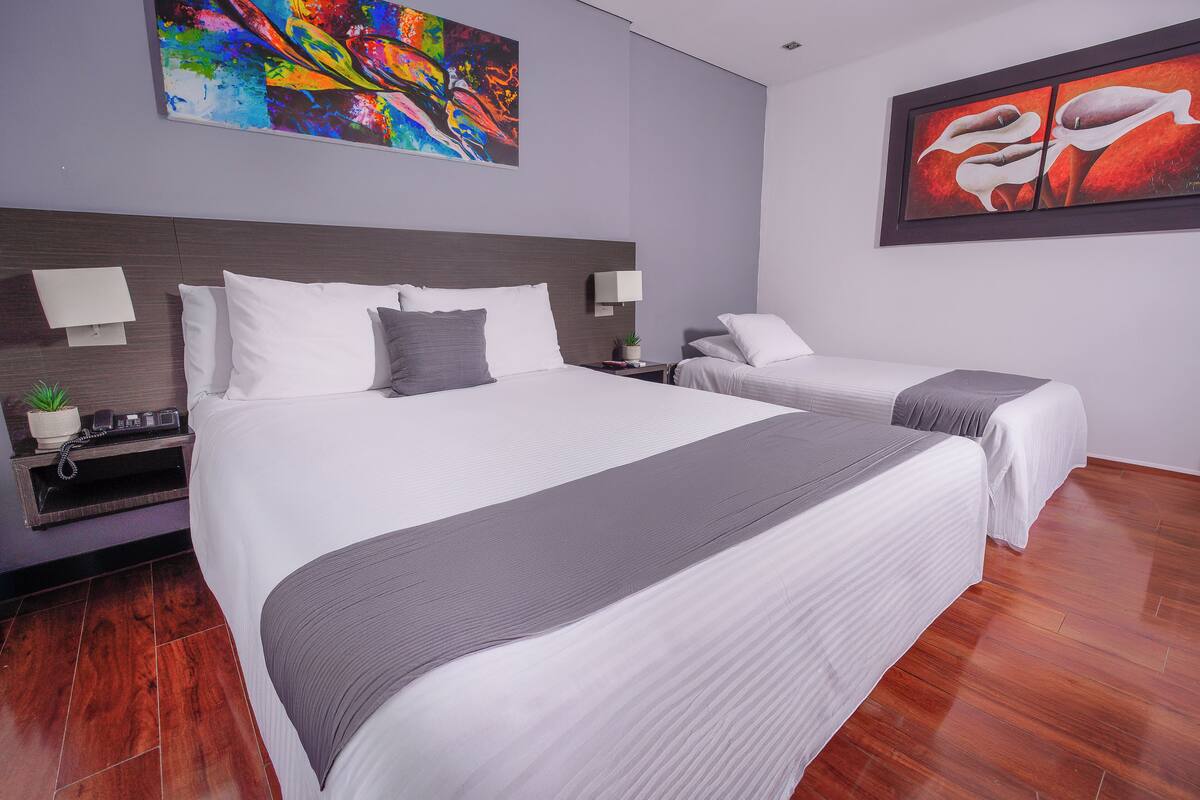 A hotel room with two beds, a large painting on the wall, and a wooden floor.