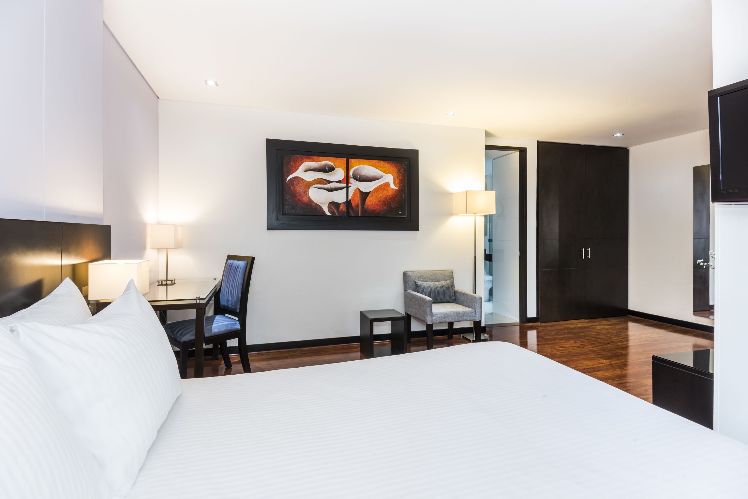 Een hotelkamer met een groot bed, een bureau met stoel, een kleine tafel, een lamp en een schilderij aan de muur.